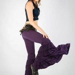May include: A woman wearing a purple and black striped bell bottom pants with a ruffled hem. The pants are made of a soft, stretchy fabric and have a comfortable fit.