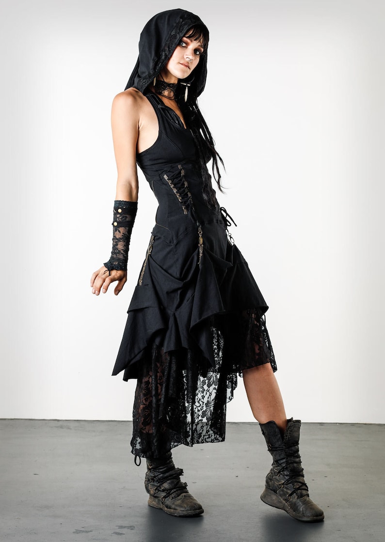 May include: A black hooded dress with a lace overlay and a corset-style bodice. The dress has a layered skirt with a high-low hemline. The model is wearing black boots.