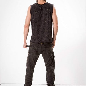 May include: A person wearing a black sleeveless shirt with a geometric pattern and black cargo pants with multiple buckles and straps.