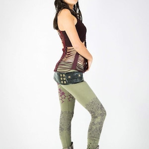 May include: A woman wearing a burgundy tank top with a black leather belt with metal accents and green leggings with a purple floral pattern. She is wearing brown boots.