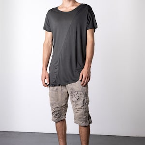 May include: A dark gray t-shirt with an asymmetrical design, paired with tan cargo shorts featuring dark floral patterns. The outfit is completed with black high-top sneakers, creating a casual, urban style.
