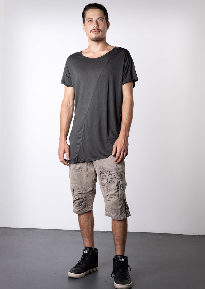May include: A dark gray t-shirt with an asymmetrical design, paired with tan cargo shorts featuring dark floral patterns. The outfit is completed with black high-top sneakers, creating a casual, urban style.