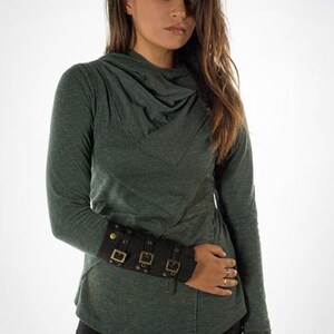 May include: A green long-sleeved shirt with a cowl neck and a black leather cuff with gold buckles on the left wrist.