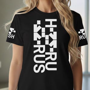 May include: A black t-shirt with white text reading "H-RUS" down the front. Small white text is on the sleeves. The person is wearing blue jeans. The shirt is made of a soft material.
