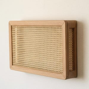 Può includere: Mobile da parete rettangolare in legno con pannello frontale in canna intrecciata. L'armadio ha una cornice in legno marrone chiaro e un inserto in canna di colore naturale. Il design è minimalista e moderno, adatto per riporre o esporre.