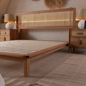 May include: A wooden bed frame with a woven headboard and footboard. The headboard has a rectangular woven panel with a light behind it. The bed frame is made of light brown wood and has a slatted base. Two matching nightstands with lamps are on either side.