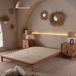 Könnte beinhalten: Ein hellbrauner Holzbettenrahmen mit Lattenrost. Zwei passende Nachttische mit Lampen flankieren das Bett. Der Raum hat eine neutrale Farbpalette mit dekorativen Wandakzenten. Das Bett ist etwa 200 cm lang.