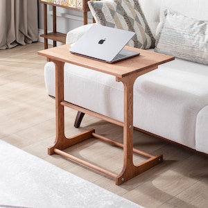 May include: A wooden side table with a rectangular top and a lower shelf. The table is made of light brown wood and has a simple, modern design. A silver laptop is placed on the table. The table is 28 inches tall.
