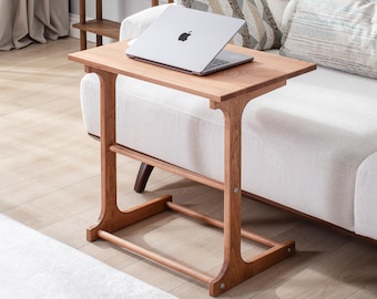 May include: A wooden side table with a rectangular top and a lower shelf. The table is made of light brown wood and has a simple, modern design. A silver laptop is placed on the table. The table is 28 inches tall.
