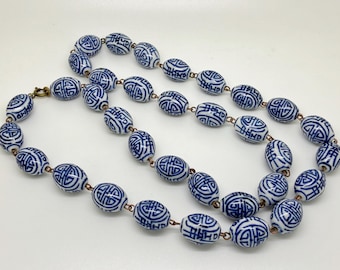May include: A necklace featuring oval-shaped beads with a blue and white pattern. The beads are strung together with copper-colored links and a brass clasp. The necklace is a piece of jewelry.