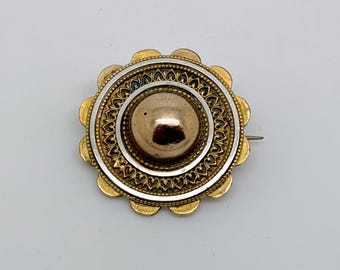 May include: A vintage brooch with a gold-tone scalloped edge and a central gold-colored dome. The brooch features a silver-colored ring with intricate detailing and a pin closure on the back. The design is circular and ornate.
