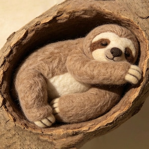 May include: A handcrafted, plush sloth nestled in a wooden tree hollow. The sloth is light brown with a cream-colored belly and a dark brown face. It is curled up, appearing asleep, with its arms and legs tucked in. The tree hollow is made of textured, brown wood.