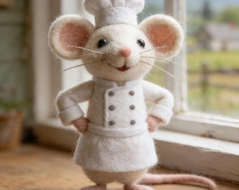 May include: A white felt mouse figurine dressed as a chef, wearing a chef's hat and uniform with small gray buttons. The mouse has pink ears, paws, and a long tail. It stands on a wooden surface near a window.