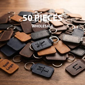 May include: A large pile of rectangular leather keychains in various shades of brown, black, and navy blue, each featuring a metal split ring. Some keychains are embossed with monograms or the text 'YOUR LOGO'. The image includes the text '50 PIECES WHOLESALE'.