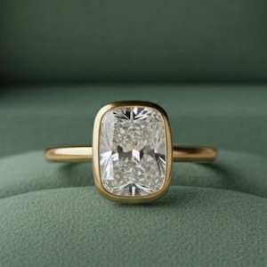 May include: A gold ring with a large, rectangular, clear gemstone is displayed inside a green velvet jewelry box. The box is open, revealing the ring and the words "NOVA JEWELS" in gold lettering.