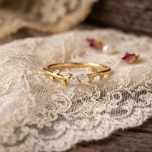 May include: A gold ring featuring a delicate branch design with two marquise-cut clear stones set in the center. The band is crafted from polished gold metal and mimics the appearance of small leaves and twigs extending along the finger.