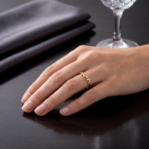 May include: A gold ring featuring a delicate leaf-shaped band design. The ring is adorned with two small, clear marquise-cut stones set within the metal leaves, creating a subtle and refined appearance on the finger.