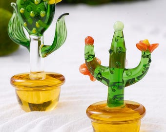 May include: Two glass cactus sculptures. One has a heart-shaped body with yellow and red flowers. The other has a three-branched body with orange and yellow flowers. Both are in yellow pots.