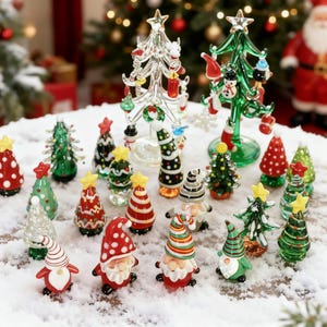 May include: A selection of miniature glass Christmas trees and gnome figurines in various colours, including red, green, and clear. Some trees have star toppers. The scene is set on a snowy surface.