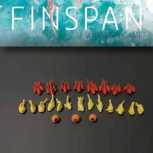 Könnte beinhalten: Eine Sammlung kleiner Spielsteine, bestehend aus acht roten fischförmigen Figuren, dreizehn gelben fischförmigen Figuren und drei runden orangefarbenen Spielsteinen mit schwarzer Mitte. Der Text FINSPAN A WINGSPAN GAME steht oben im Bild.