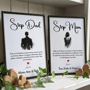 May include: Two framed prints with black frames, one reading "Step Dad" and the other "Step Mom". Each print features a silhouette and a heartfelt message. Wooden heart decorations and greenery accent the display.