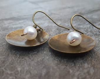 May include: A pair of brass earrings with a small white pearl hanging from each. The earrings are in the shape of a small, flat disc.