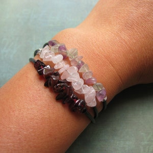 Pu&ograve; includere: Tre braccialetti sovrapposti con chip di pietre preziose di diversi colori. Lo strato superiore &egrave; verde e viola, lo strato intermedio &egrave; rosa e lo strato inferiore &egrave; rosso scuro.