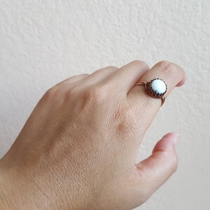 May include: A white ring with a black border and a white stone in the center. The ring is on a person's finger.