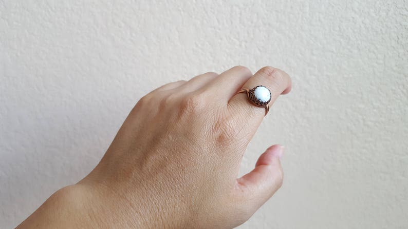 May include: A white ring with a black border and a white stone in the center. The ring is on a person's finger.