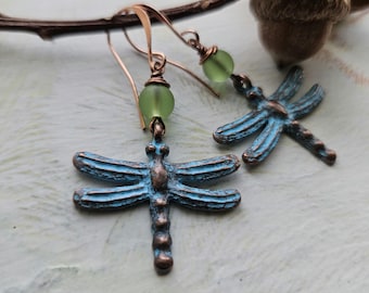 May include: A pair of dragonfly earrings with a distressed blue finish and green glass beads. The earrings are made of copper and have a simple, elegant design.