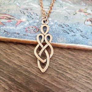 May include: A copper-colored Celtic knot pendant necklace. The pendant is a long, thin, intricate knot design.