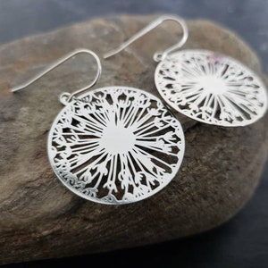 May include: A pair of silver dangle earrings with a delicate, circular design that resembles a dandelion. The earrings have a simple, elegant style.