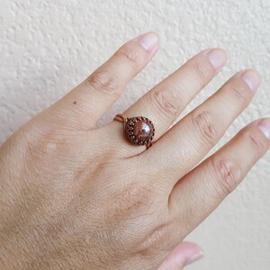 May include: A copper wire ring with a brown stone set in the center. The stone has a speckled pattern.