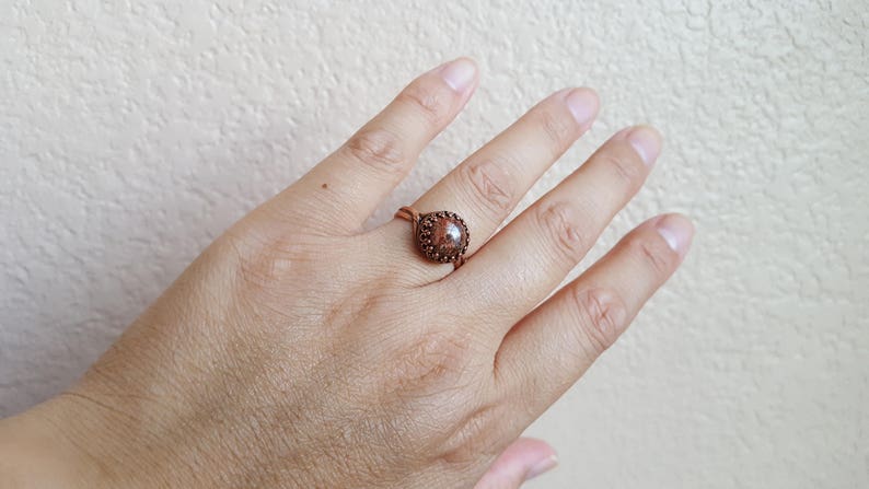 May include: A copper wire ring with a brown stone set in the center. The stone has a speckled pattern.
