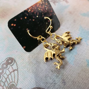 May include: A pair of gold-toned dragon earrings. Each earring features a detailed dragon design with wings and a tail.