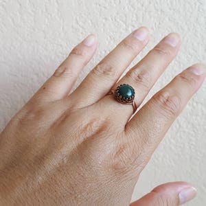 May include: A copper ring with a dark green gemstone set in a decorative bezel.