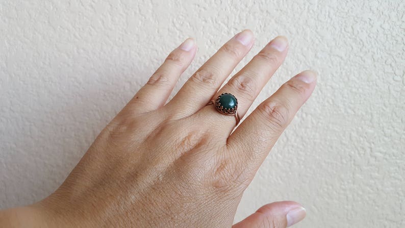 May include: A copper ring with a dark green gemstone set in a decorative bezel.