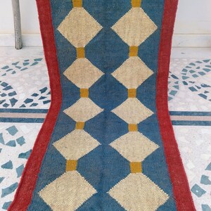 May include: A blue and cream-colored runner rug with a repeating diamond pattern. The diamonds are cream-colored and outlined in yellow, set against a blue background. The rug has a red border.