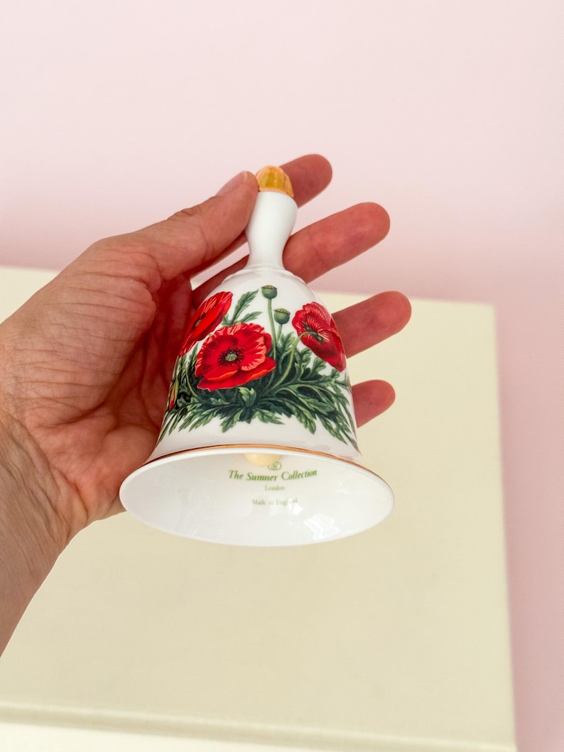 Puede incluir: Campana de cer&aacute;mica blanca con asa dorada y dise&ntilde;o floral de amapolas. La campana presenta amapolas rojas con hojas verdes y el texto "The Summer Collection London". Hecho en Inglaterra.