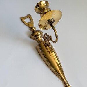 May include: A vintage brass candle holder and bottle opener set. The candle holder features a circular base and a curved arm. The bottle opener has a decorative top. Both items have a polished finish.