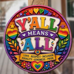 May include: A round wooden hanging sign featuring a rainbow-colored border and the text Y'ALL MEANS ALL in large letters. Below, a banner displays the words LOVE, RESPECT, INCLUSION, EQUALITY, KINDNESS, PRIDE, surrounded by colorful hearts and flowers.