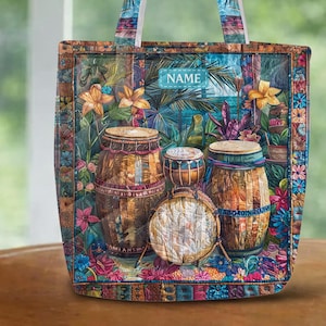 May include: A colorful tote bag featuring a tropical design with drums, flowers, and the word "NAME". The bag has a rectangular shape with a matching patterned handle. The background shows a beach scene.