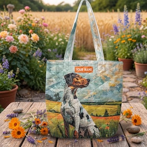 May include: A quilted tote bag featuring a dog illustration in a field setting. The bag has a light blue background with a dog illustration and the text "YOUR NAME" on a rectangular label. The bag has matching handles.