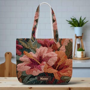 May include: A floral tote bag featuring a large hibiscus flower design in shades of pink, orange, and red. The bag has a white handle and a brown leather patch with the word "Name". The background is a dark green and brown floral pattern.