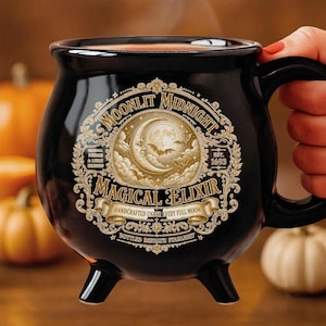 May include: A black cauldron-shaped mug with three feet and a handle. The front features a gold-toned ornate circular graphic with a crescent moon, bats, and text reading Moonlit Midnight Magical Elixir, Est. 1693, Handcrafted Under Every Full Moon.