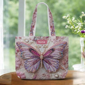 May include: A pink tote bag featuring a large butterfly design with intricate details. The butterfly has purple, pink, and blue wings, embellished with pearls and gems. The bag has a white handle and the word "Name" on a pink label.