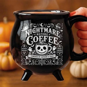May include: A black ceramic cauldron-shaped mug with three small feet. The front features white graphic text reading "NIGHTMARE BEFORE COFFEE," "HAUNTED MORNING CLUB," "FRESHLY BREWED NIGHTMARES," "POWERED BY CAFFEINE & CHAOS," and "ESPRESSO BEFORE EXORCISM."