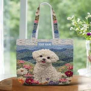 May include: A tote bag featuring a white Bichon Frise dog sitting in a field of colorful flowers. The bag has a blue and white mountain landscape background and the text "YOUR NAME" on the front. The handles are white with floral accents.