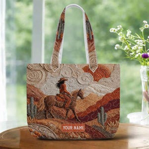 May include: Tote bag with a western-themed design. The bag features a detailed illustration of a cowgirl riding a horse through a desert landscape. The bag has a white handle and the text "YOUR NAME" is visible.