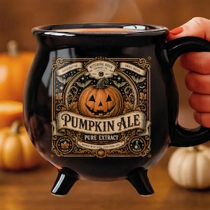 May include: A black ceramic cauldron-shaped mug with three small feet. The front features a decorative label with an orange jack-o'-lantern illustration, ornate gold borders, and the text "Witching Hour Brewing Co. Pumpkin Ale Pure Extract".